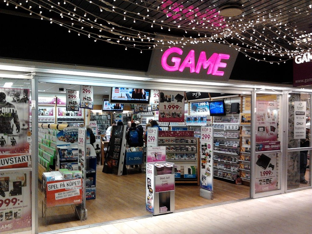 Interiör av en GAME-butik i ett köpcentrum med spelprodukter på hyllorna och kunder som tittar.